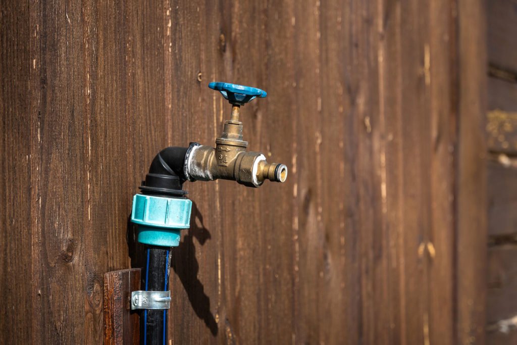 A faucet with a hose attached hangs on a brown wall.