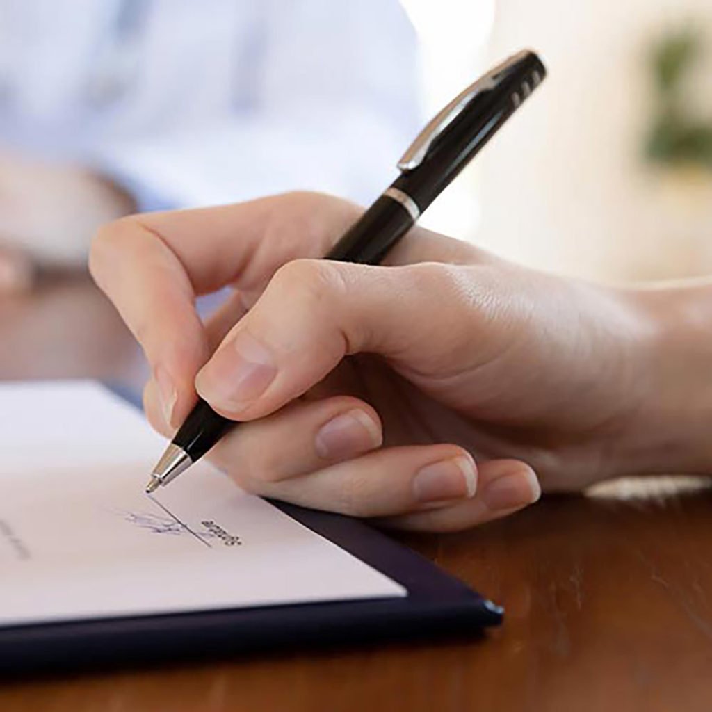 a hand holding a pen preparing to sign a document