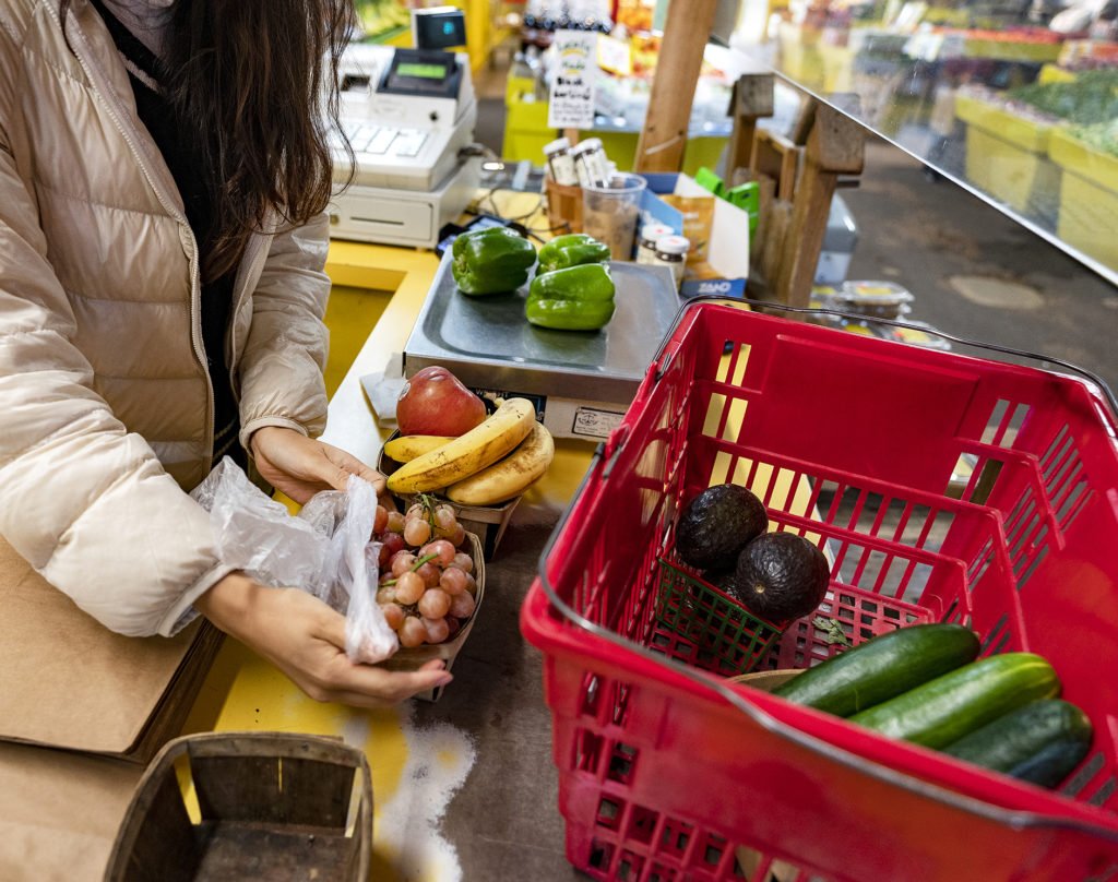 a red basket with vegetables in it and a woman's hands beside it holding grapes with bananas and tomatoes on the counter