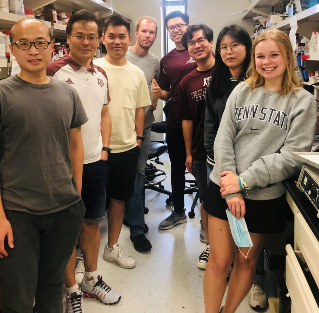 a large group of people stand on both sides of work areas in a lab.