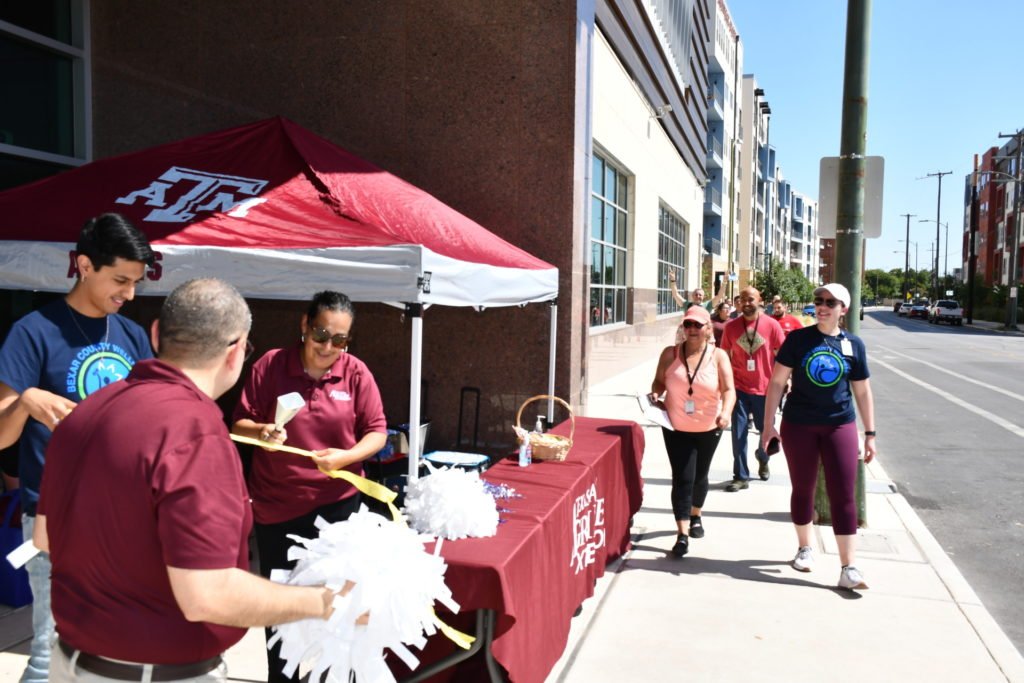 Walk Across Texas! participants come down a sidewalk in downtown San Antonio to where a table and tent are set up