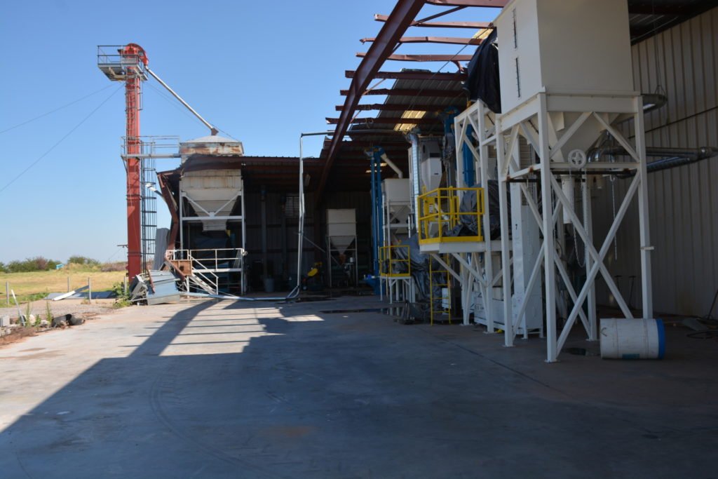 Large white pieces of equipment can be seen with blue sky above it where a tornado damaged the roof and walls.