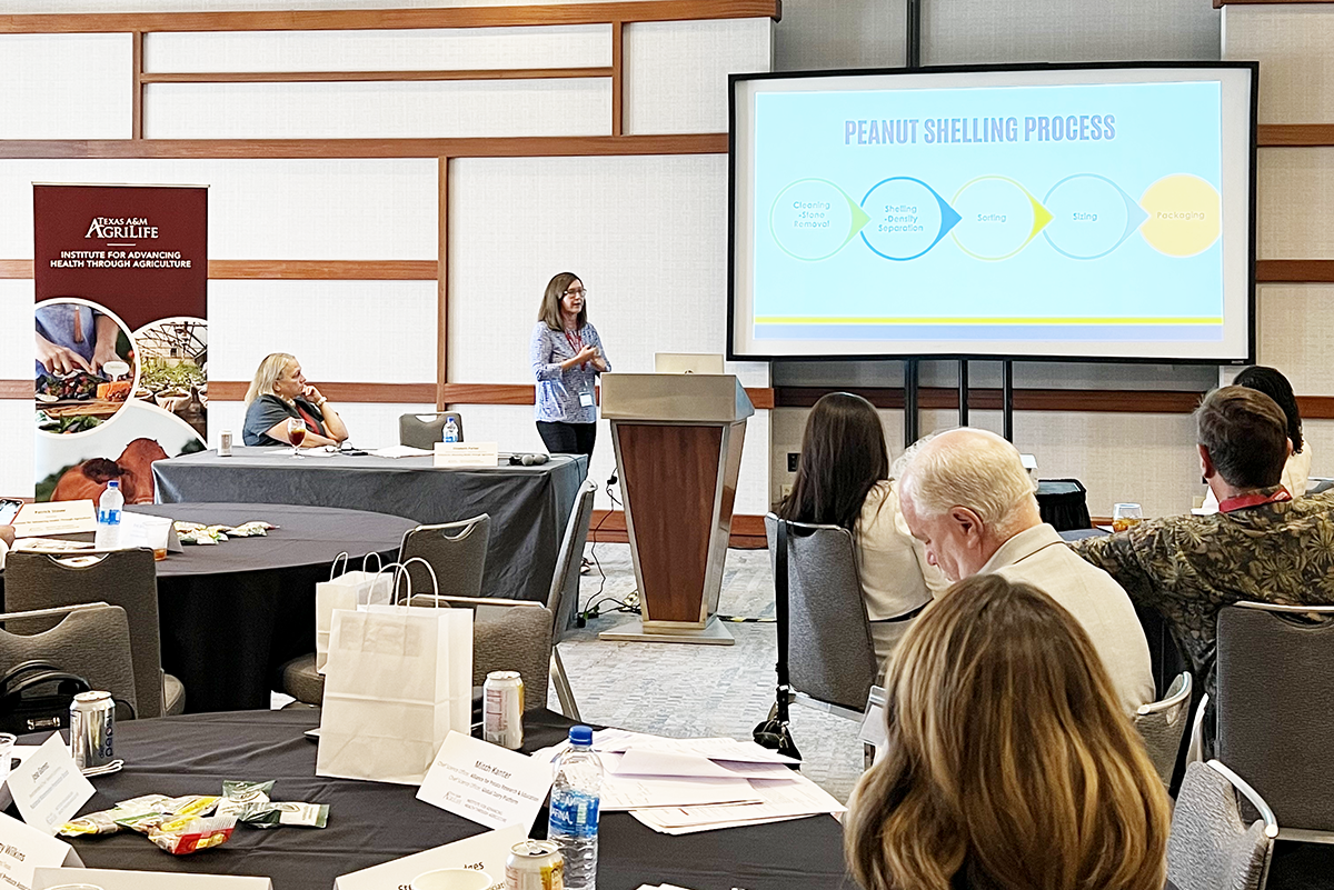 Darlene Cowart gives a slideshow presentation in a large conference hall to an audience seated at round tables in a workshop.
