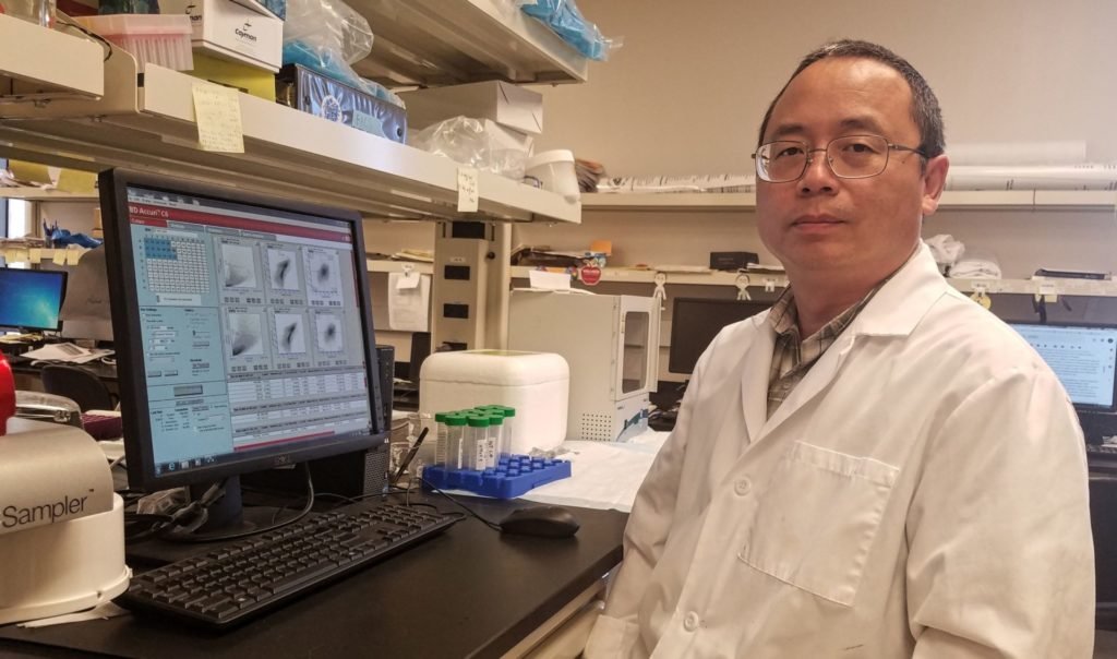 a man, Chaodong Wu, Ph.D., sits in his laboratory in front of a computer