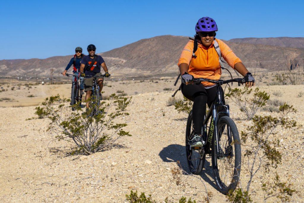 Three people riding bikes on desert-like terrain in West Texas  