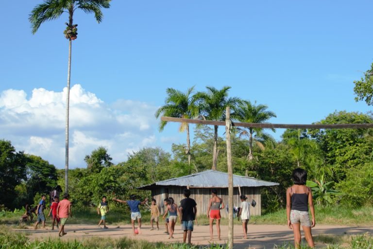 Nukak children play football on a field surrounded by chontaduro palm trees in the Agua Bonita camp.