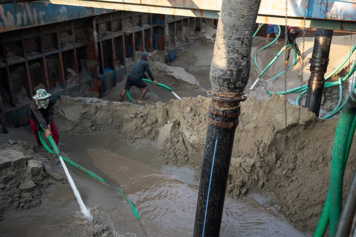 Workers spray water to suspend sand so that it can be offloaded from a barge.