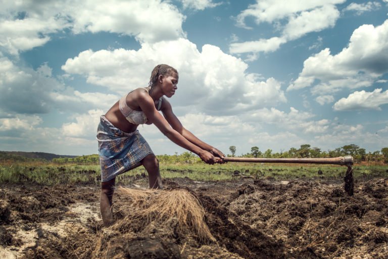 Woman cutting at the edge of a ditch with a long-handled hoe. Image © Mauro Sérgio/National Geographic Okavango Wilderness Project